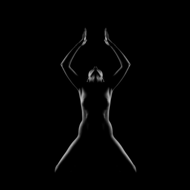Fekete-fehér, nagy kontrasztos, szimmetrikus női aktfotó. A képen a női formák vonalai hangsúlyosan vannak kiemelve, a női mellek enyhén látszanak.